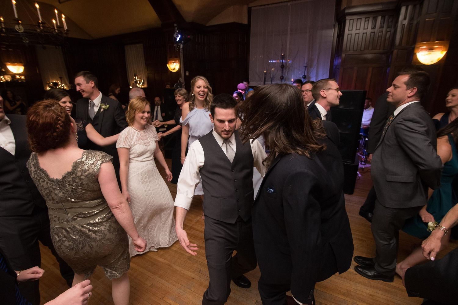 Guests dancing joyfully at an elegant wedding reception in a grand ballroom with warm lighting.