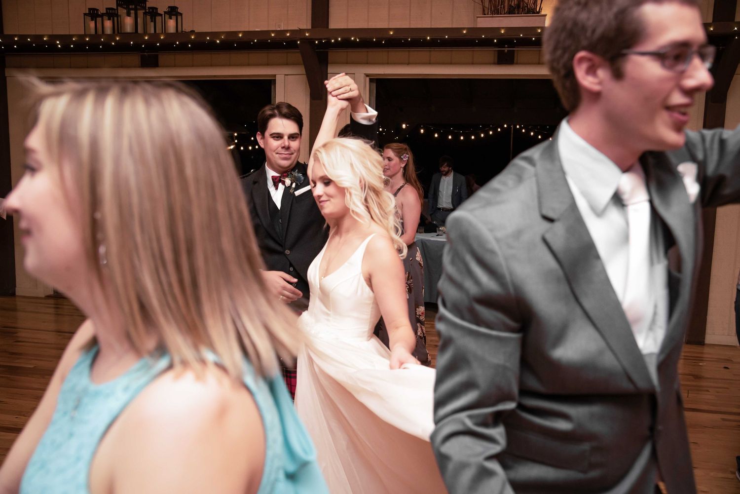 Bride in white gown dancing with groom at wedding reception in rustic venue with string lights.