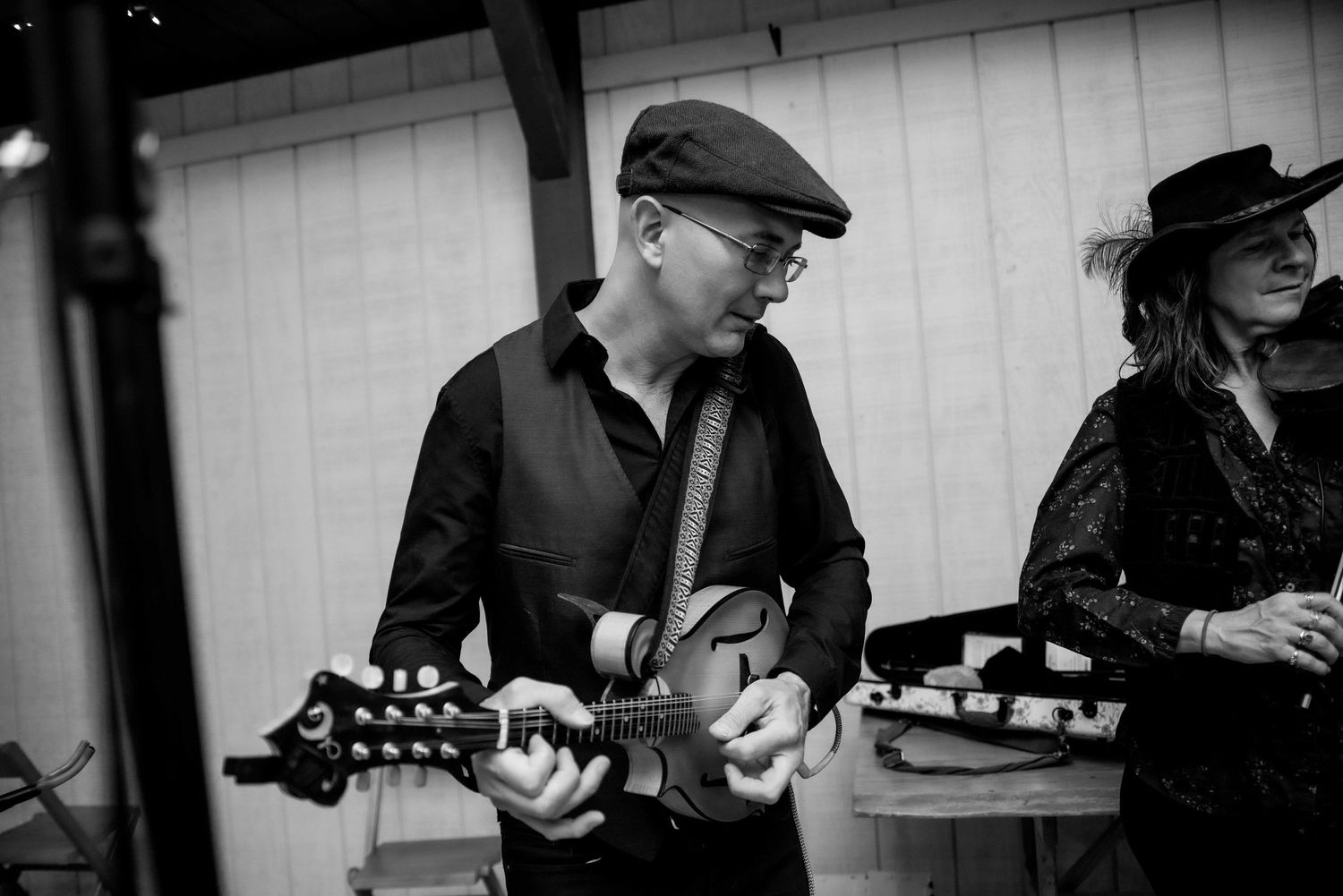 Black and white photo of a man in a flat cap playing electric guitar at an indoor music event.