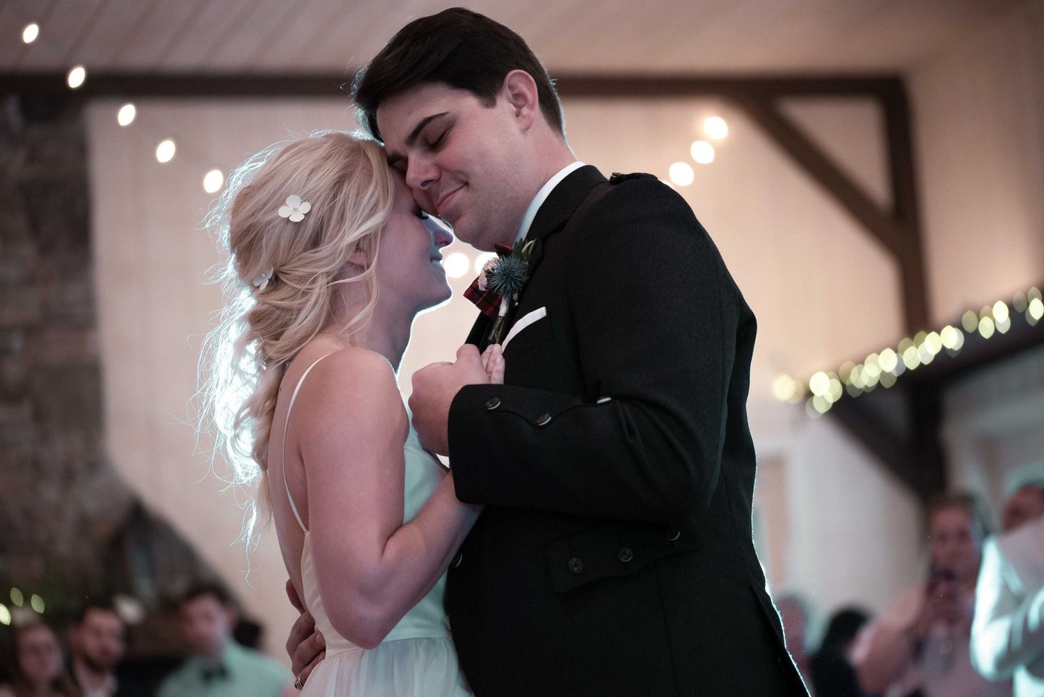 Bride and groom share their first dance at a romantic wedding reception with warm string lights in the background.