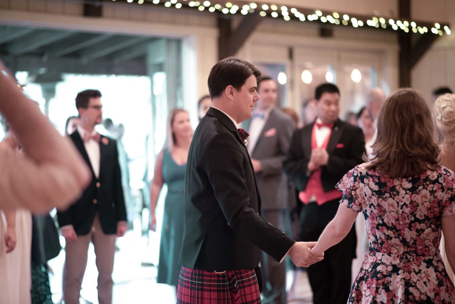 Man in kilt and bow tie dancing with woman in floral dress at elegant wedding reception.