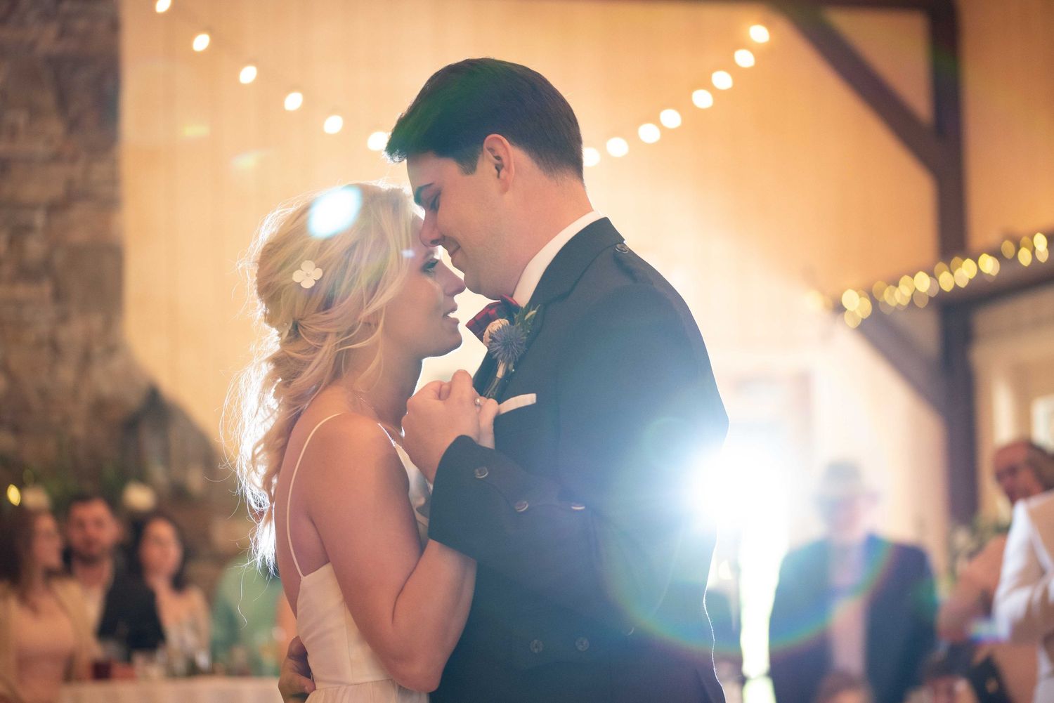 Bride and groom share their first dance at a romantic wedding reception with warm string lights glowing in the background.