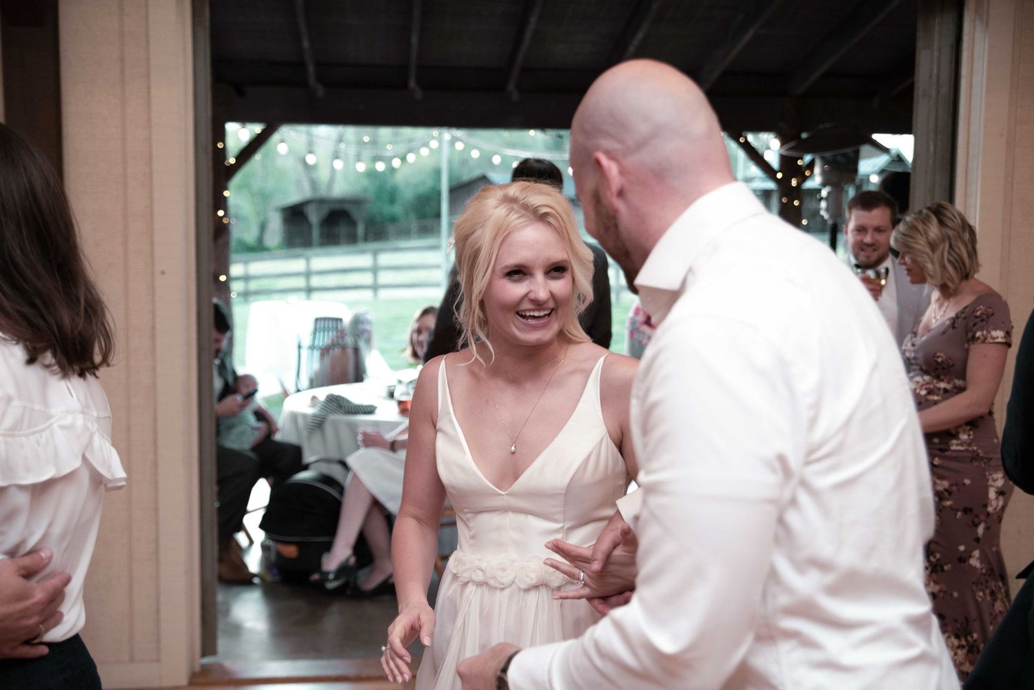 Couple sharing a joyful dance at a wedding reception, bride in blush gown smiling at bald groom in white shirt.