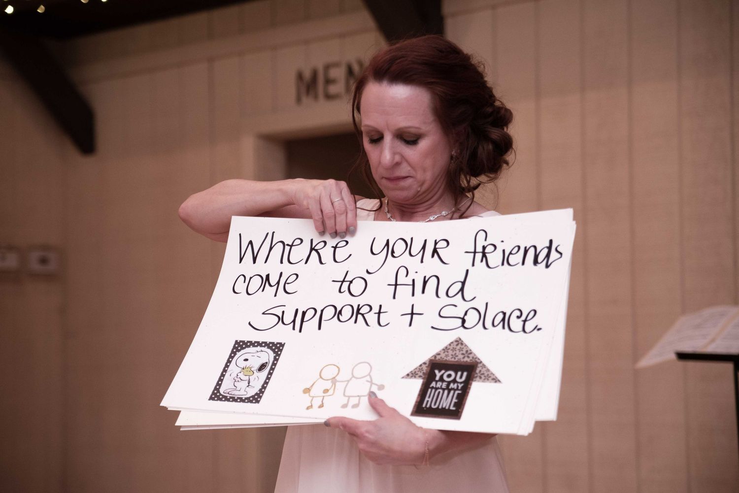 Woman holding a handmade sign reading Where your friends come to find support and solace at an indoor event.