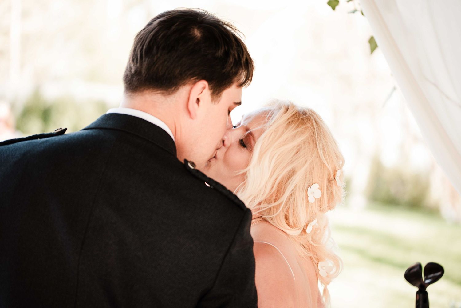 A bride and groom share their first kiss at an outdoor wedding ceremony, with the bride wearing a veil.