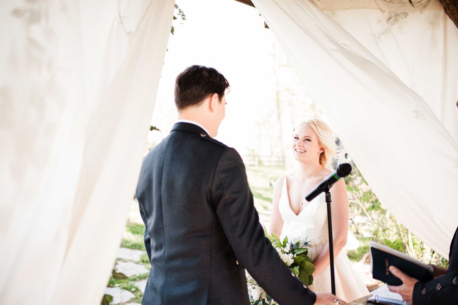 Bride smiling at groom during outdoor wedding ceremony under white draped tent.