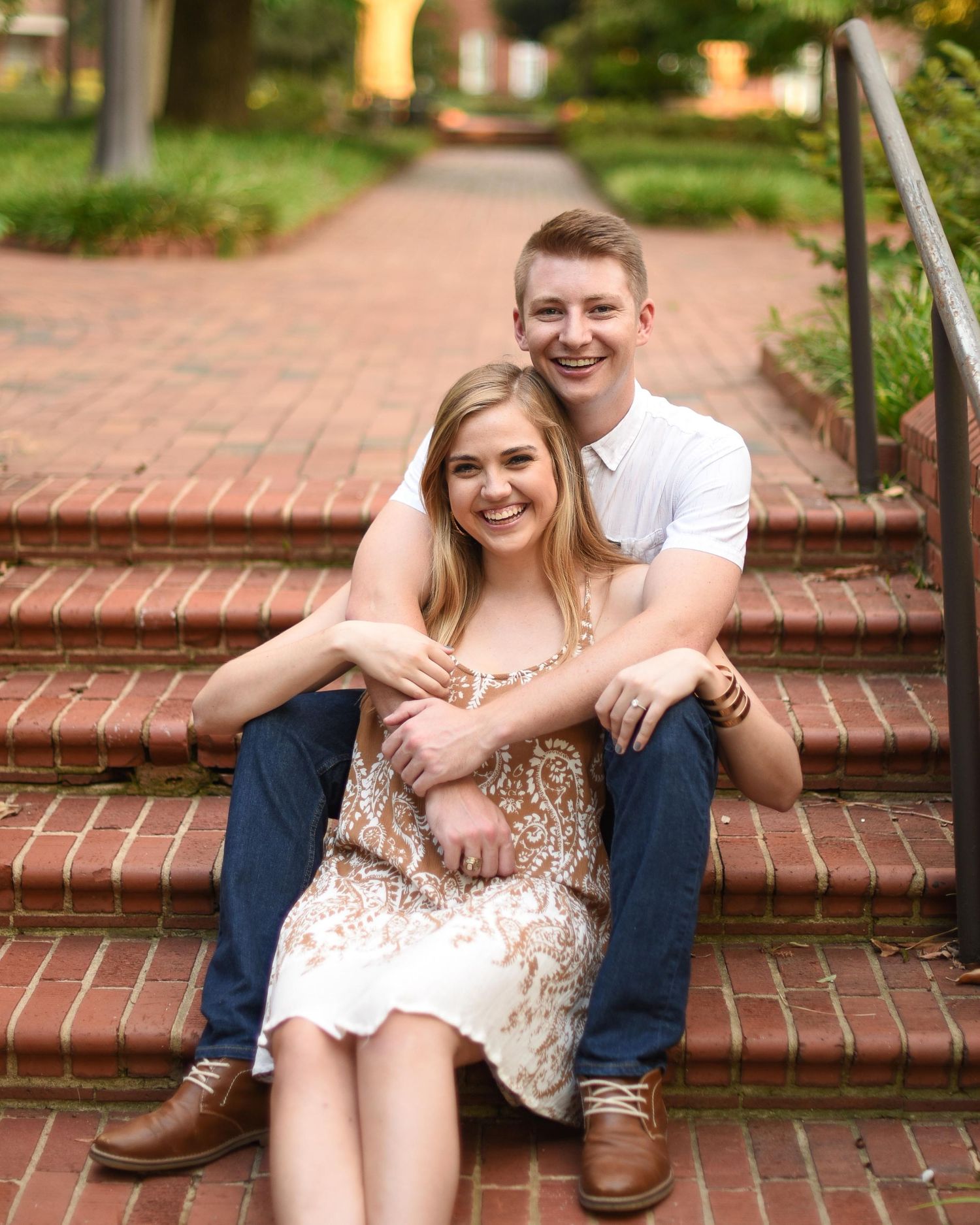 Happy couple sitting on brick steps outdoors, with the man embracing the woman from behind.