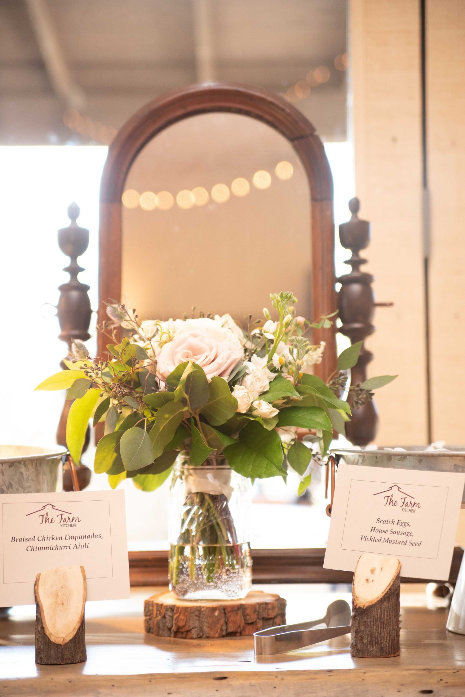 Rustic wedding reception table with pink floral centerpiece in mason jar on wood slice, vintage mirror and menu cards.