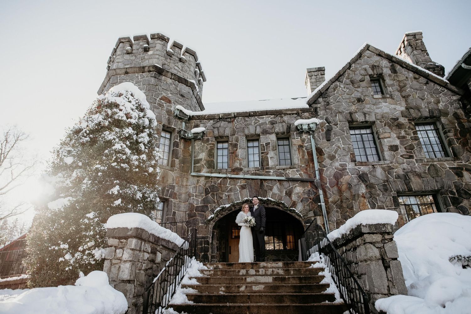 Bride and groom kissing on snowy castle steps in winter wedding portrait at stone fortress venue.