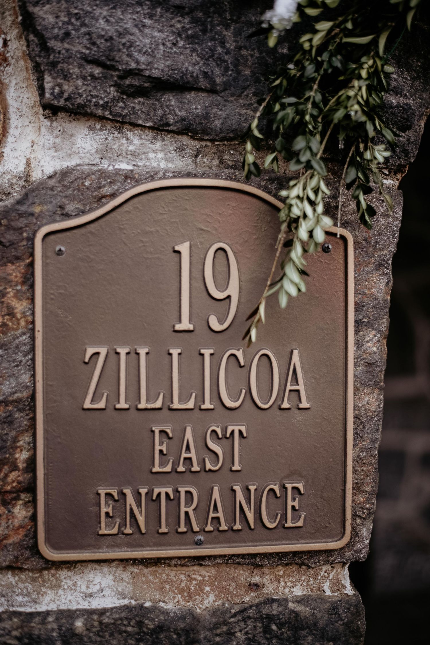 Bronze address plaque reading 19 Zillicoa East Entrance mounted on a stone wall with greenery.