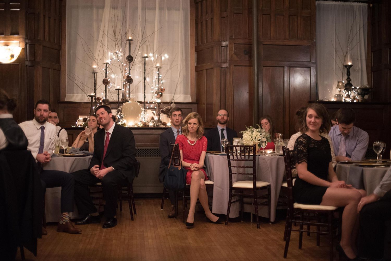 Elegantly dressed guests seated at tables in a wood-paneled banquet hall during a formal event.