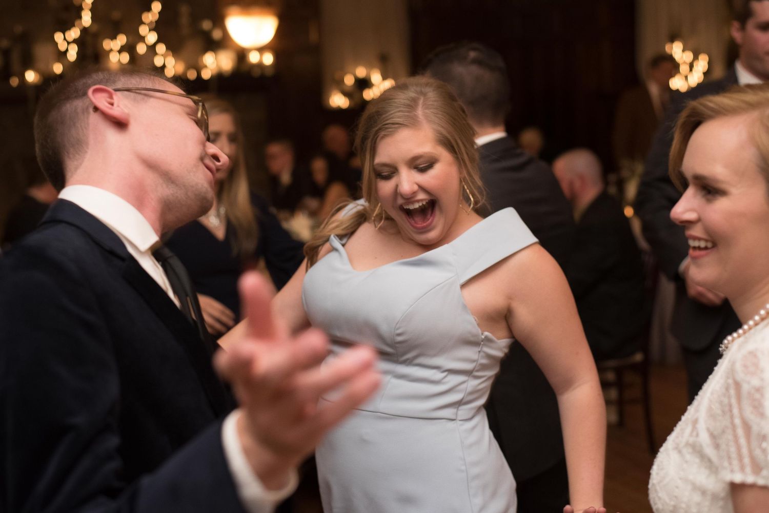 Guests laughing and dancing joyfully at an elegant wedding reception in a formal ballroom venue.