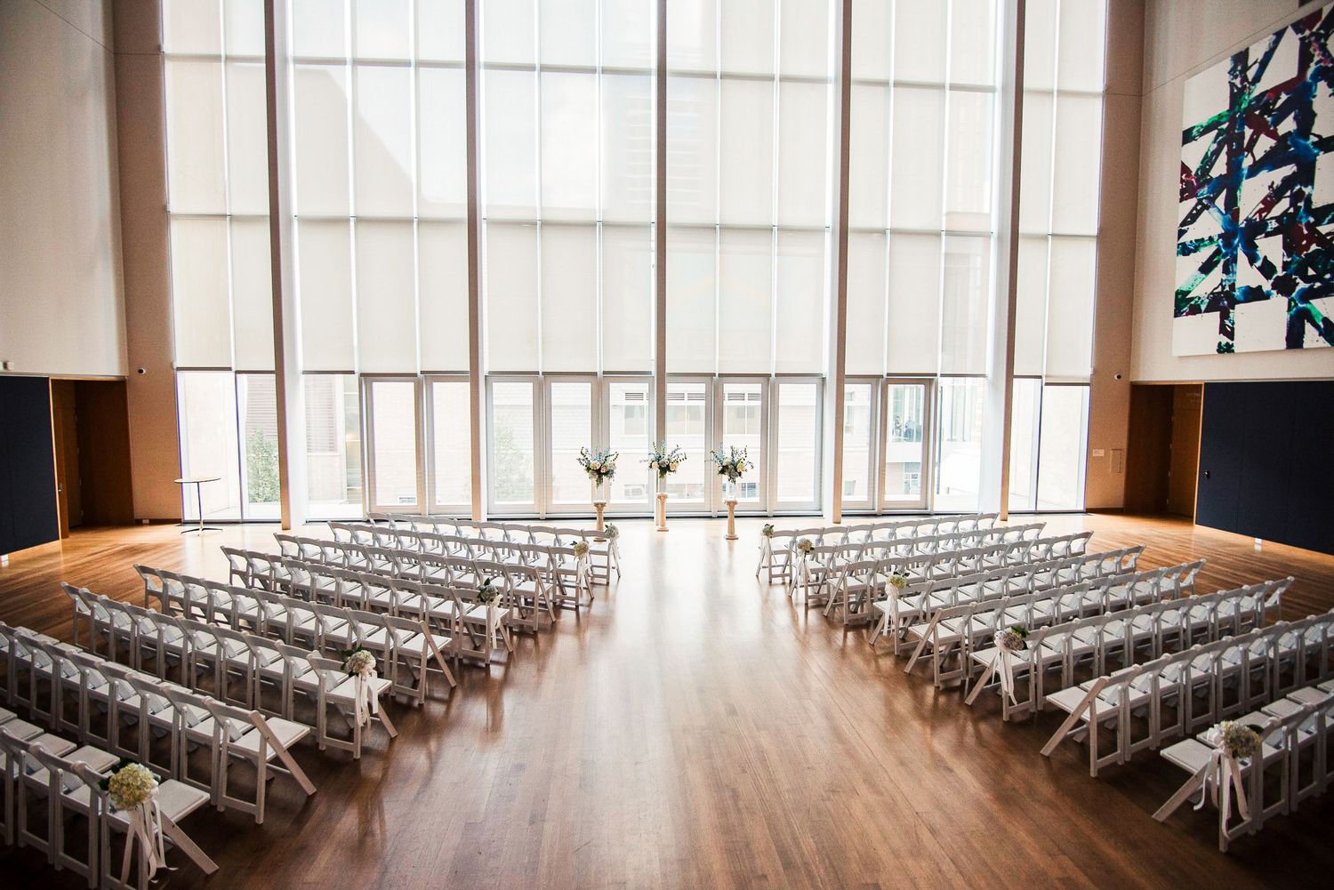 Modern wedding ceremony venue with white folding chairs, tall windows, and colorful abstract art.
