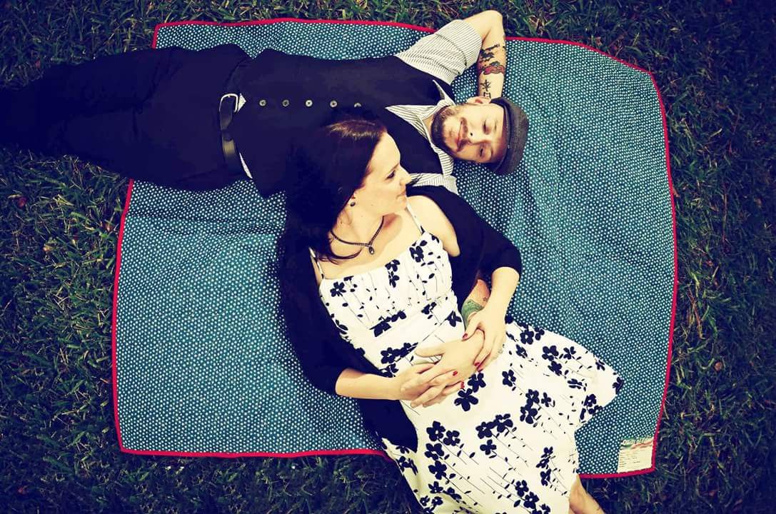 A couple lies together on a blue blanket in the grass in a charming aerial engagement photo.