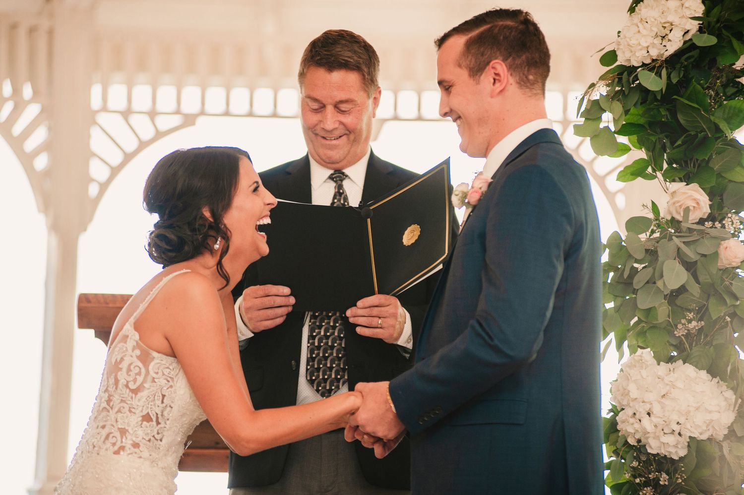Bride and groom laughing during wedding ceremony at outdoor gazebo altar.