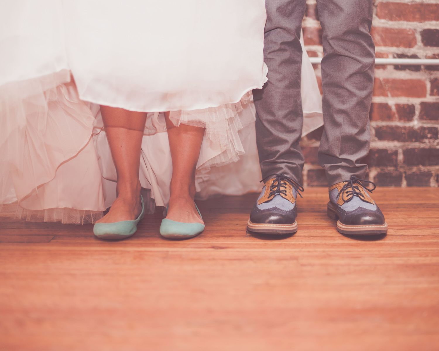 Close-up of bride in blue flats and groom in brown oxfords standing on hardwood floor.