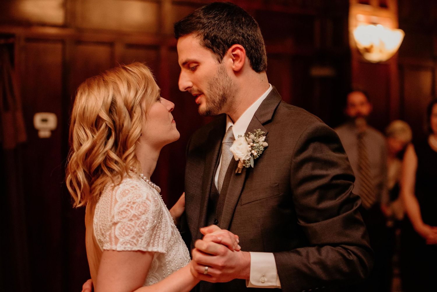 Bride and groom share their first dance, smiling at each other in a warmly lit wedding reception venue.