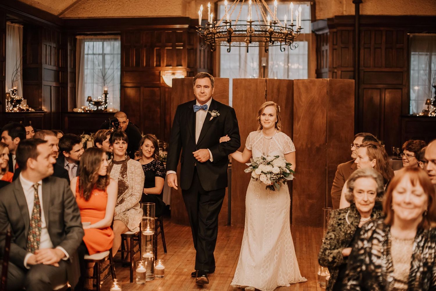 Bride and groom walk down the aisle together in an elegant wood-paneled wedding venue with candlelit decor.