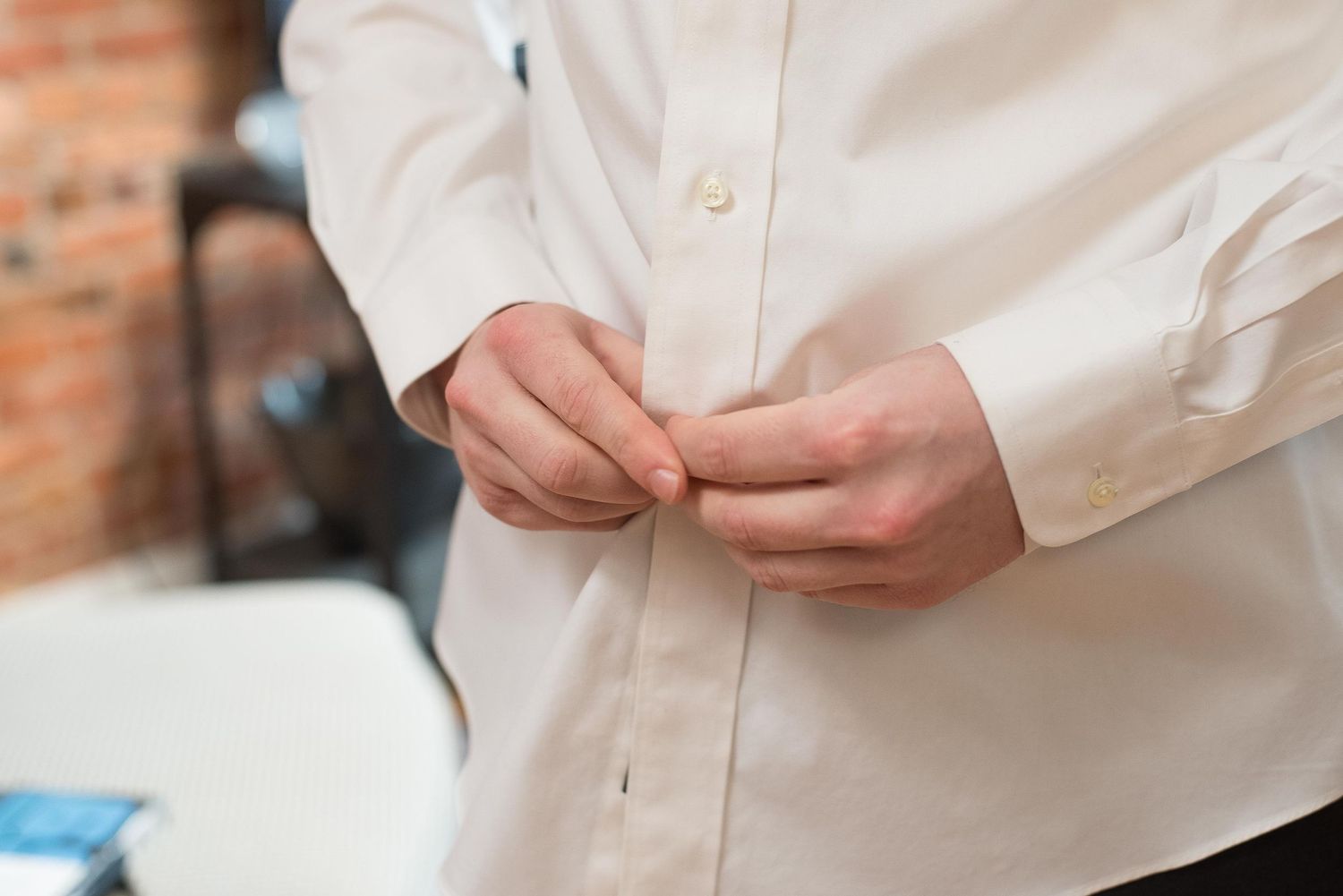 Man buttoning a white dress shirt, close-up view of hands fastening shirt buttons.