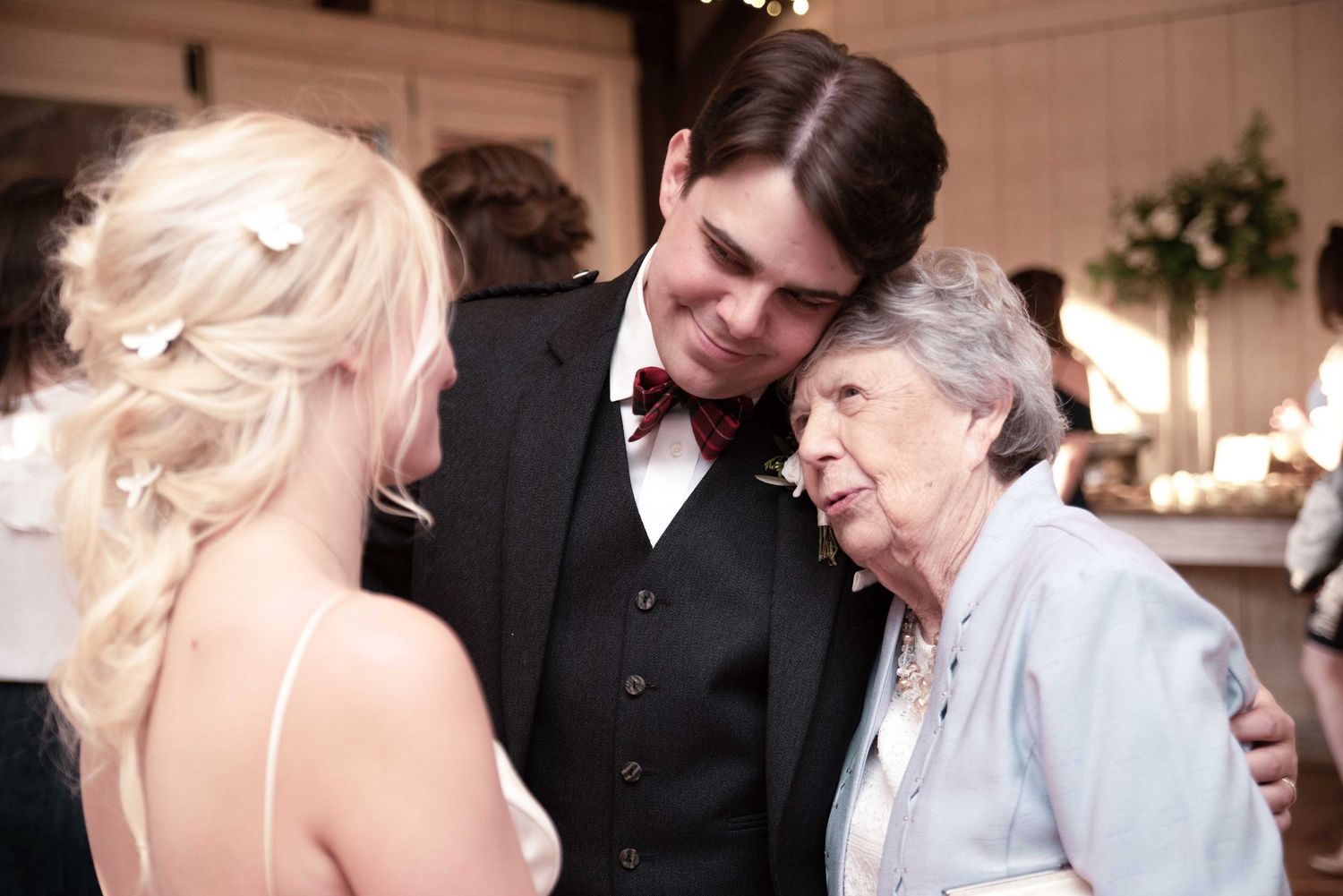 Bride and groom sharing a tender moment with elderly grandmother at wedding reception.
