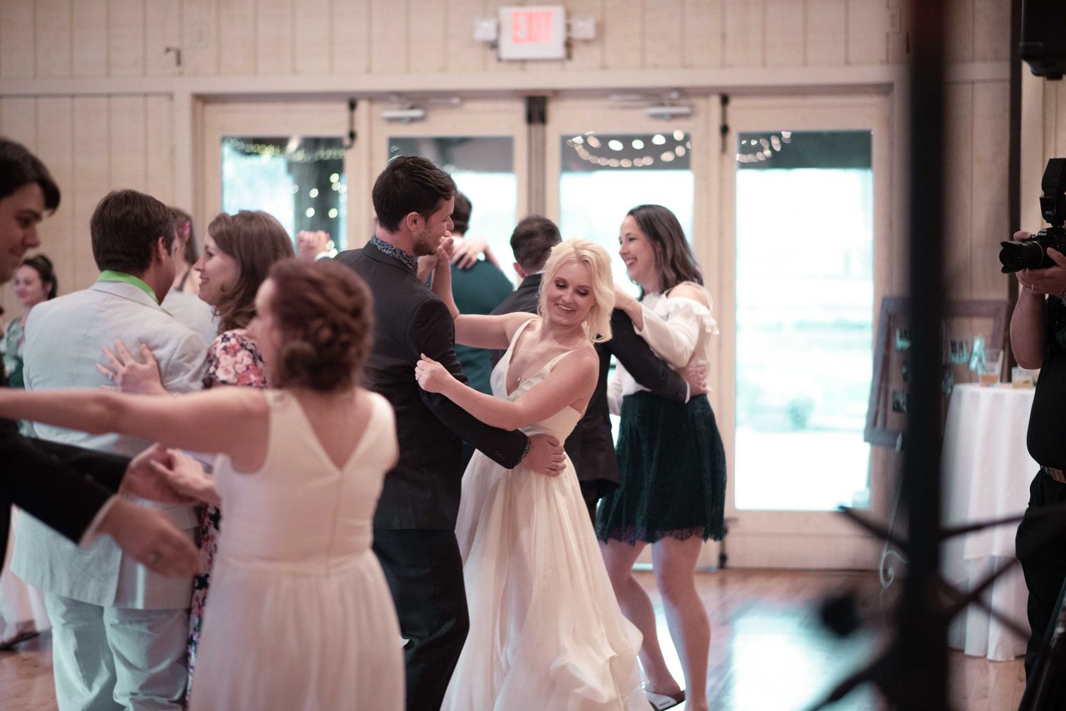 Bride and groom share a dance with guests at a wedding reception in an elegant venue.
