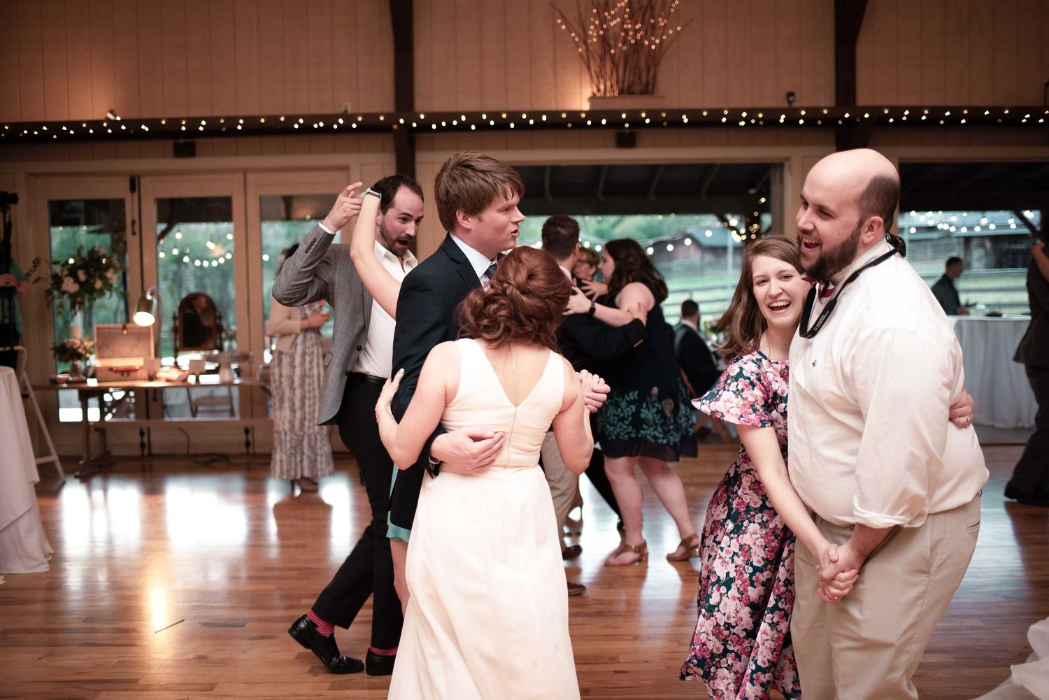 Couples dancing joyfully at a rustic wedding reception on a wooden dance floor in an elegant venue.