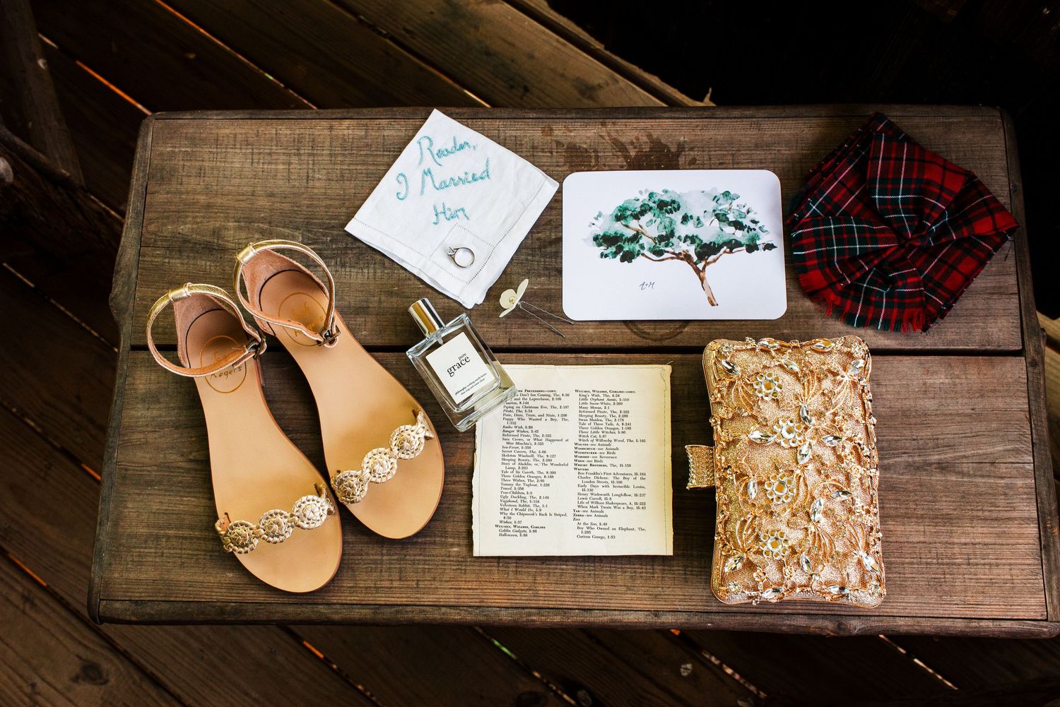 Flat lay of wedding accessories including sandals, perfume, Bible, plaid bow tie, and stationery.