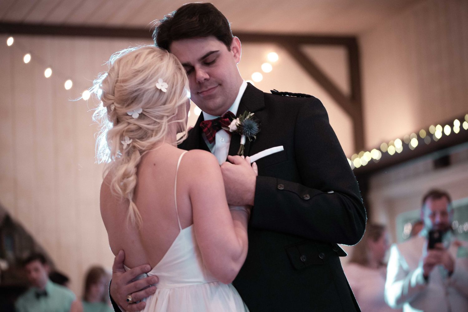Bride and groom sharing their first dance at a rustic wedding reception with warm string lights in the background.
