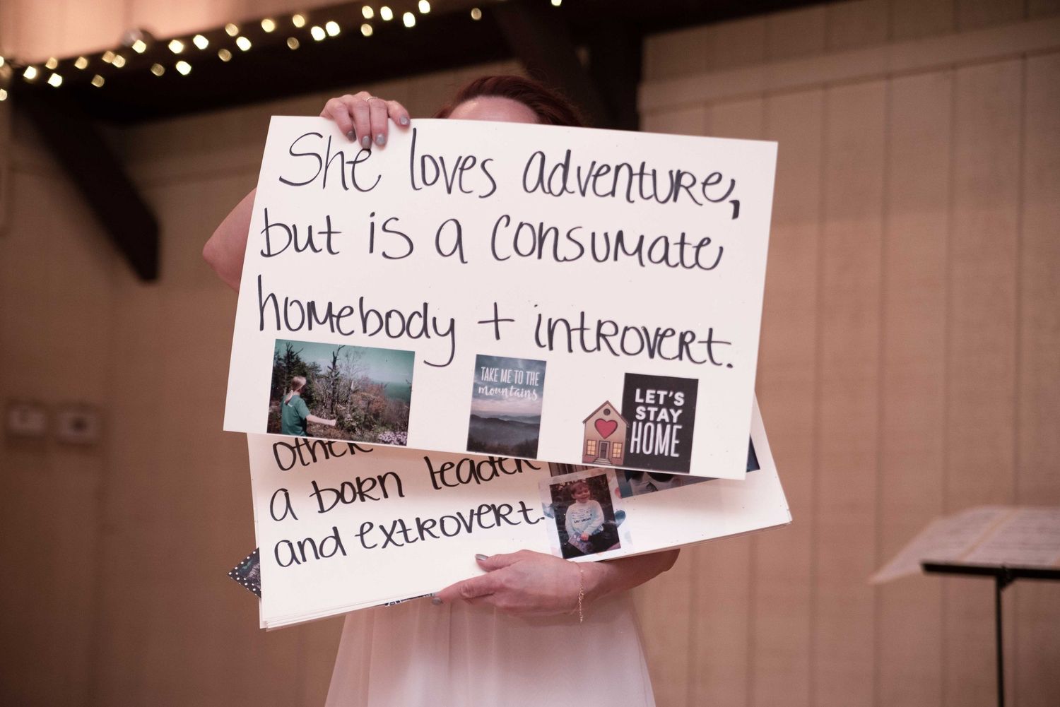 Person holds handwritten sign describing bride as homebody introvert and born leader extrovert at wedding.