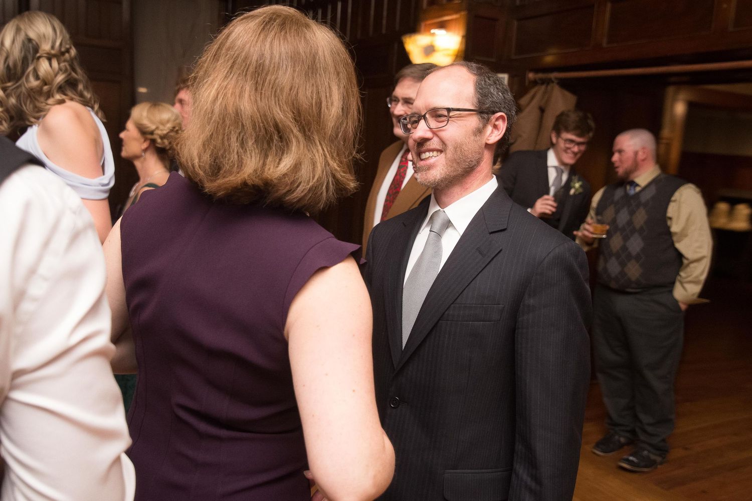 Man in dark suit and gray tie conversing with woman in purple dress at formal indoor event.