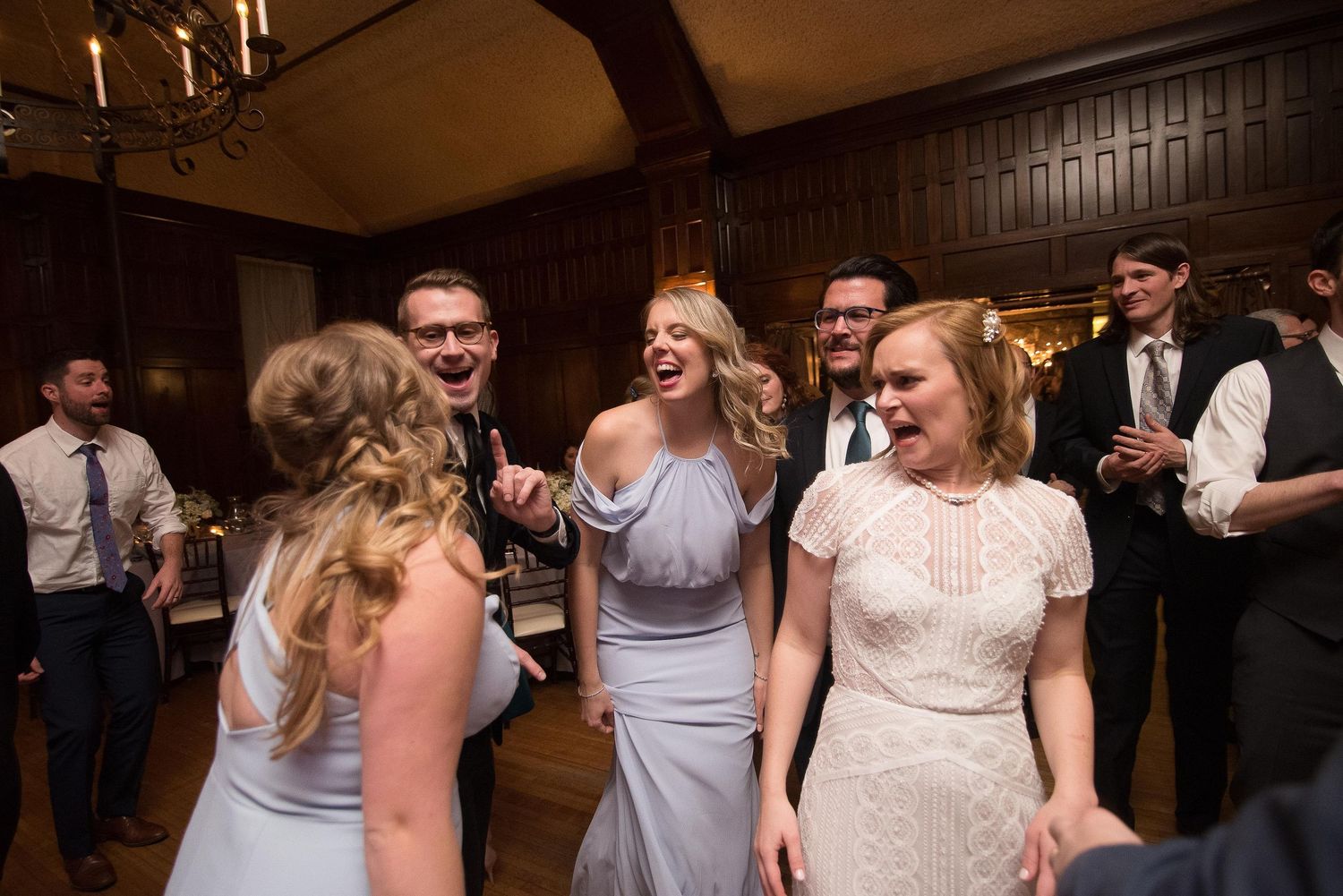 Wedding guests laughing and dancing joyfully at a reception, bridesmaids in blue dresses celebrating with friends.
