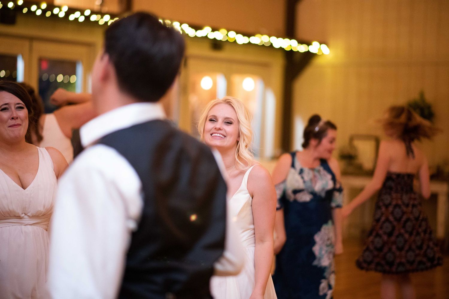 Guests dancing and smiling at a warmly lit wedding reception in a rustic venue.
