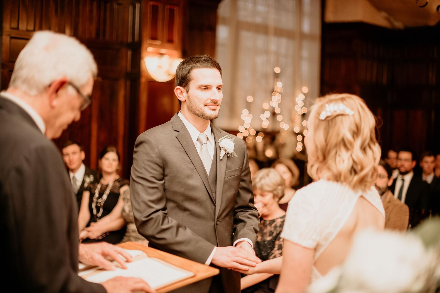 Groom smiling at bride during wedding ceremony at elegant venue with guests seated in background.