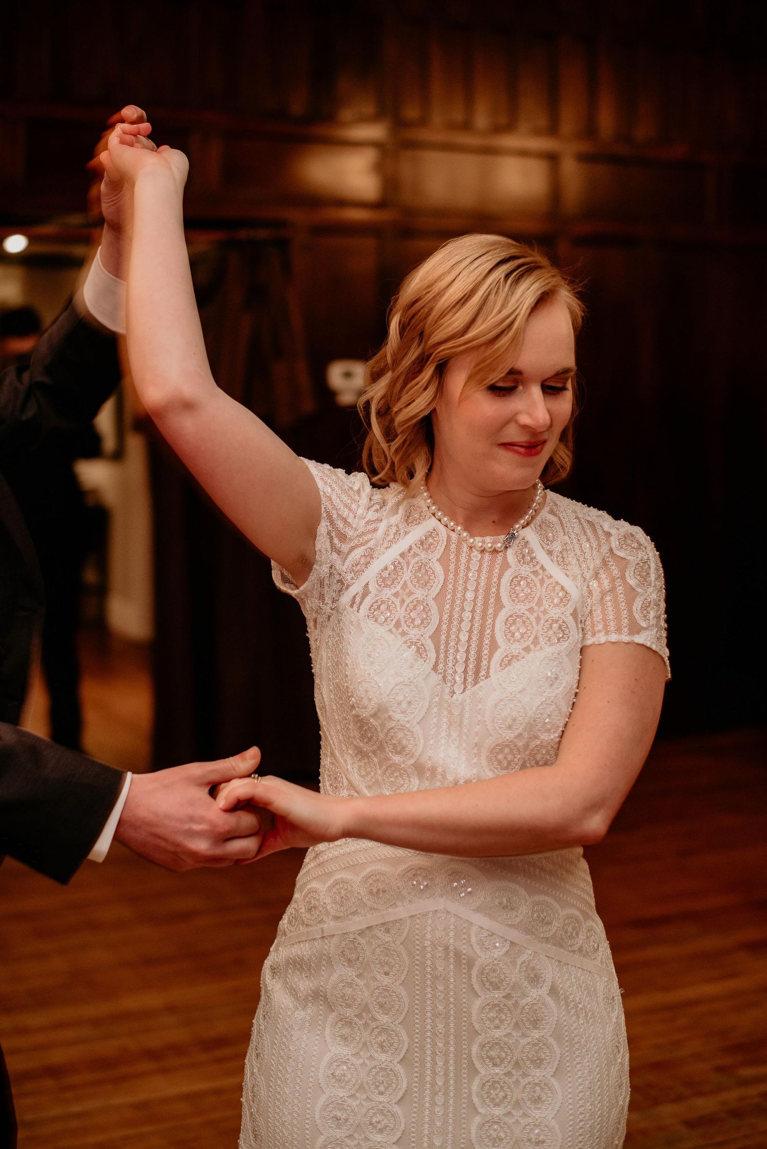 Bride in lace wedding gown dancing elegantly, raising her arm during first dance at wedding reception.