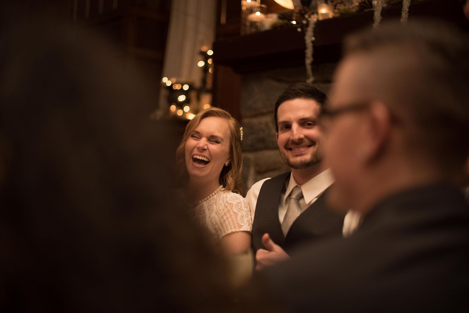 A laughing bride and groom share a joyful moment at their dimly lit, warmly decorated wedding reception.