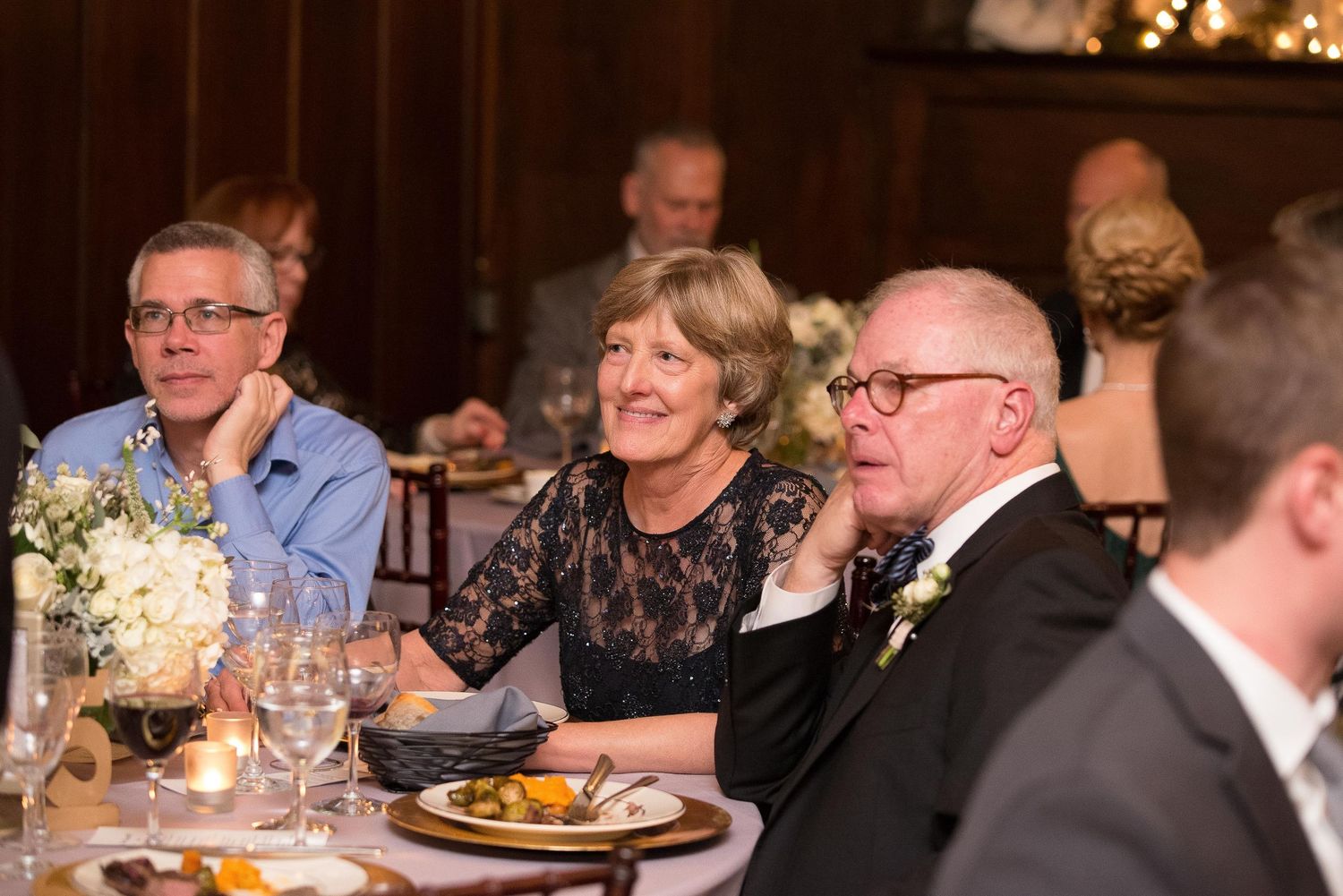 Elderly guests smile and chat at a formal wedding reception dinner, seated at an elegantly decorated table.