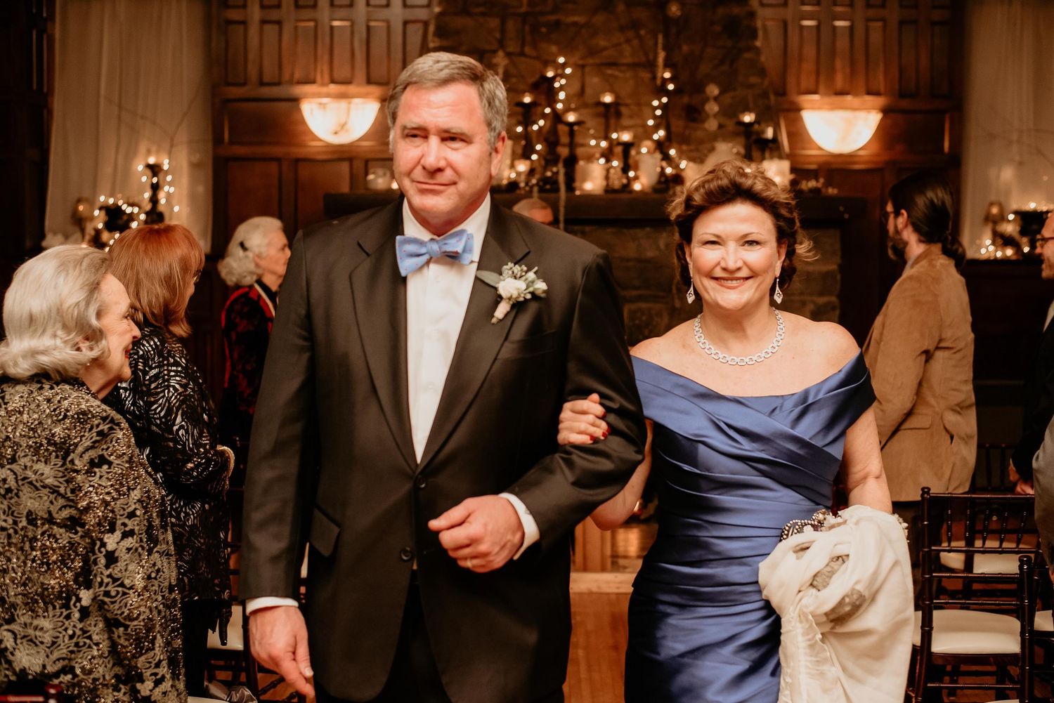 Elegant couple in formal attire walking together at a wedding reception in a warmly lit venue.