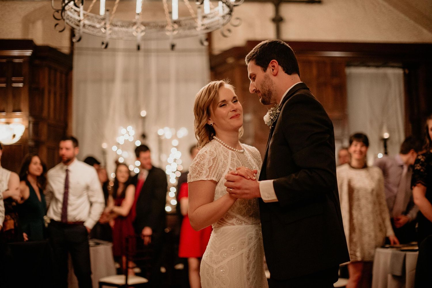 Couple sharing their first dance at an elegant wedding reception with guests and sparkling lights in the background.