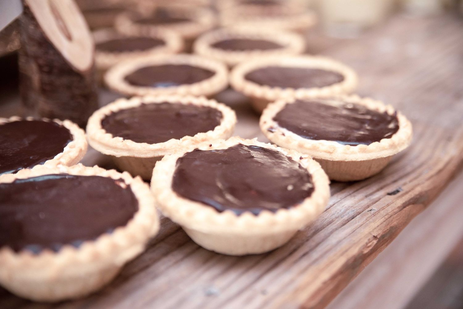 Rustic chocolate ganache tarts in pastry shells arranged on a wooden board at a wedding reception dessert table.