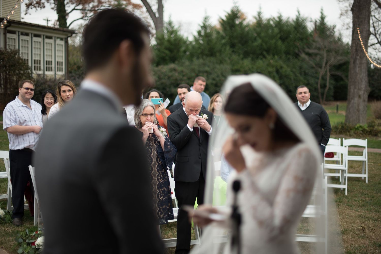 Emotional outdoor wedding ceremony with bride in veil and guests applauding in background.