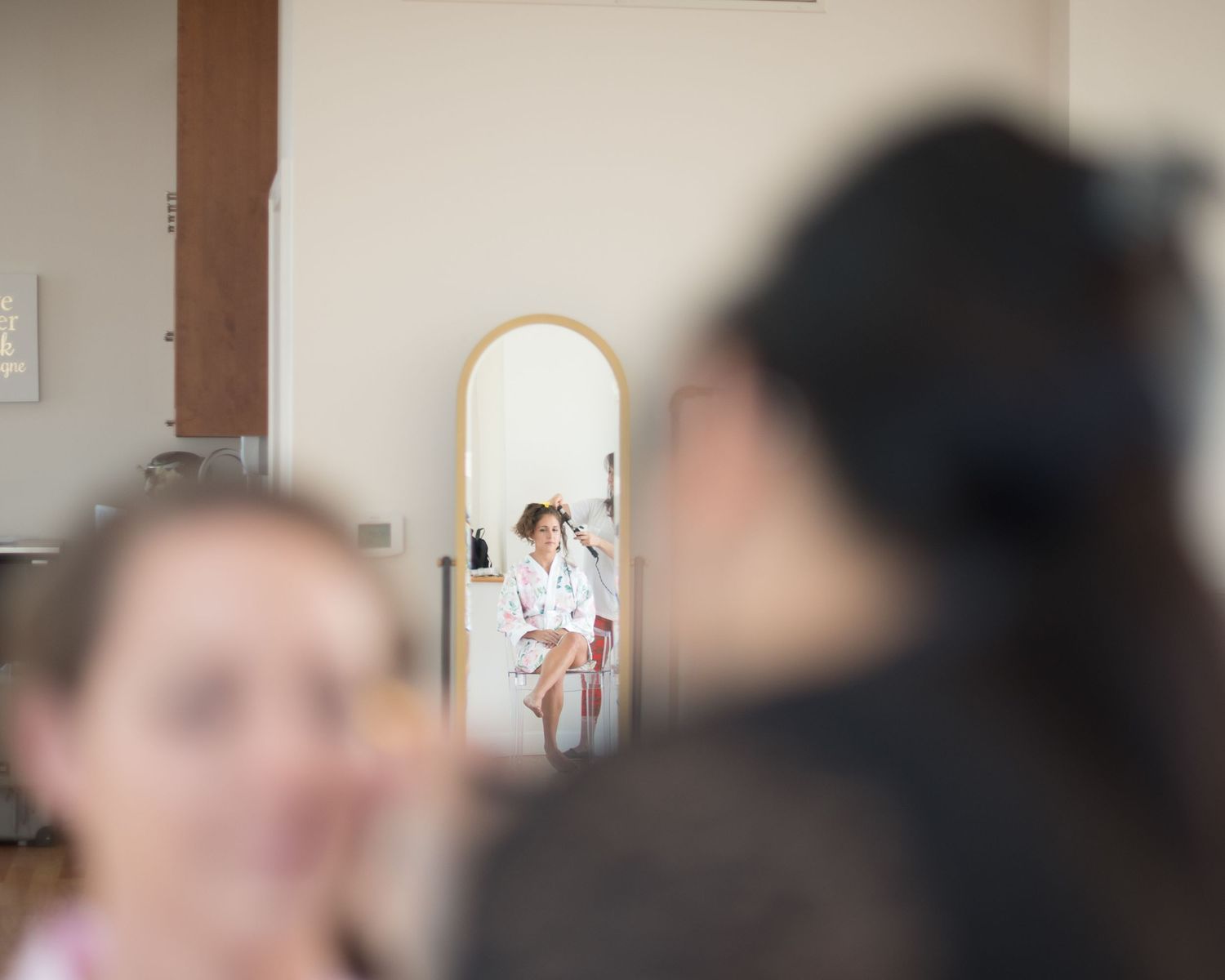 Bride in white robe reflected in full-length mirror during wedding morning preparation getting ready.