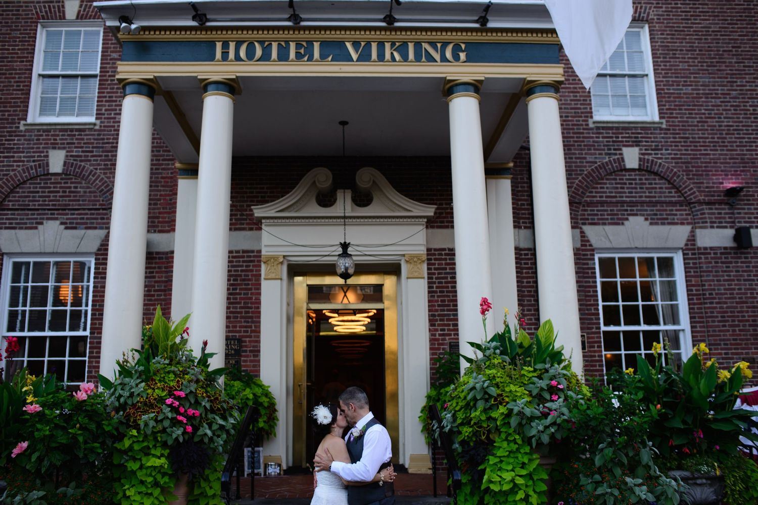 Bride and groom embrace at the entrance of Hotel Viking, surrounded by lush floral arrangements.