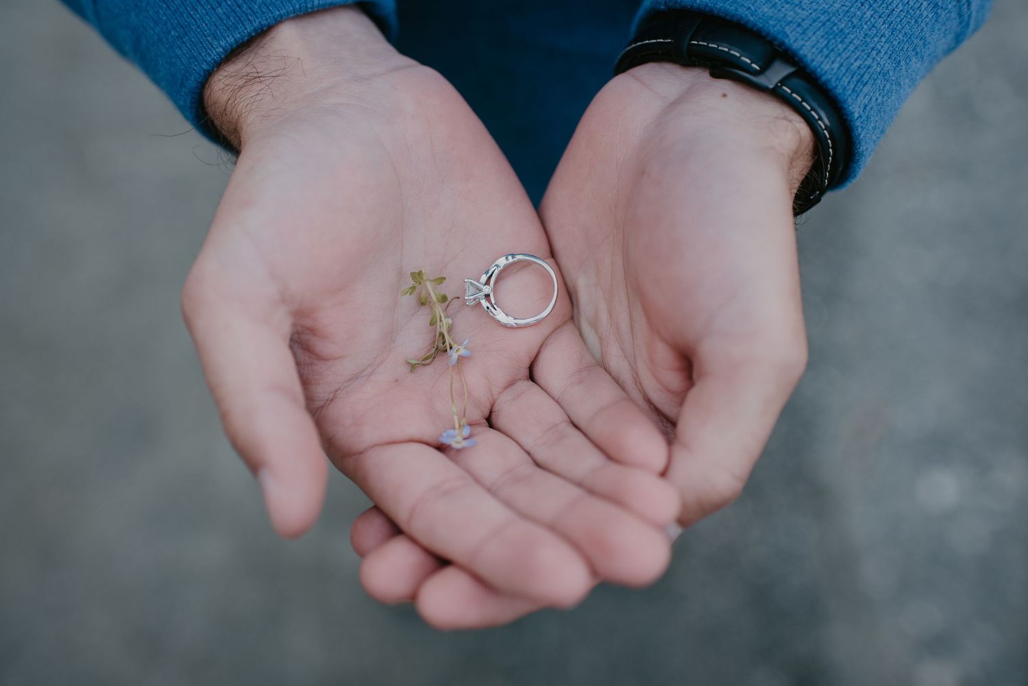 Groom holds wedding rings and a small cross charm in his open palms before the ceremony.