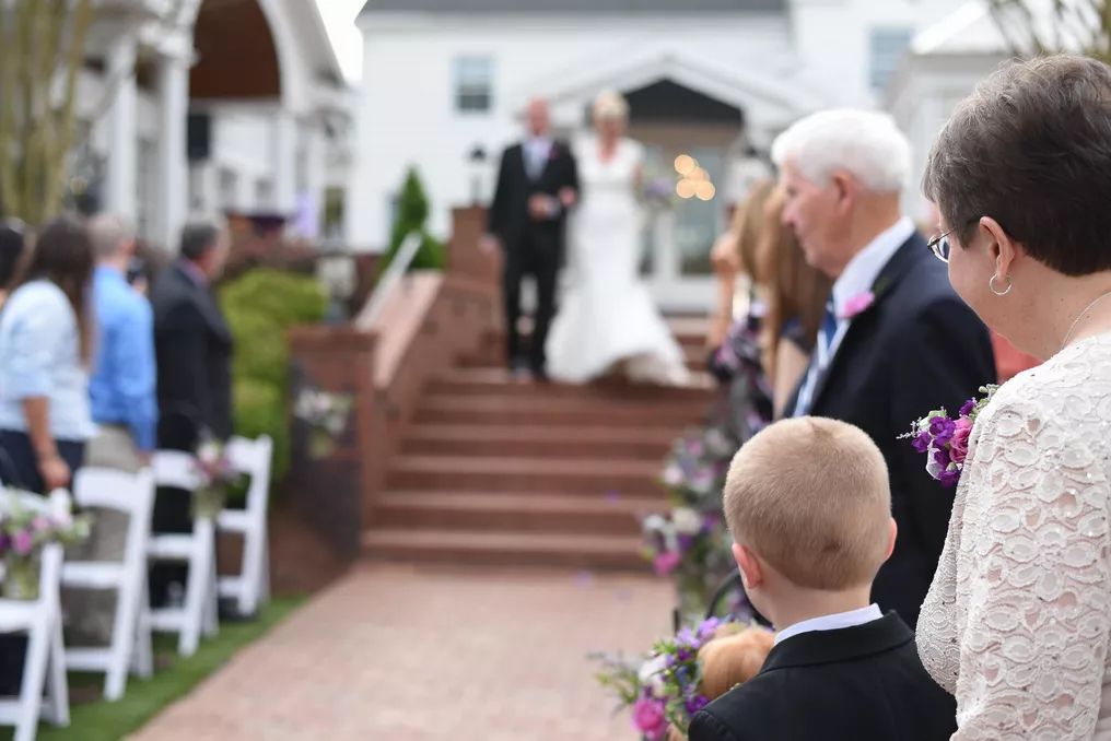 Guests watch as a bride descends outdoor stairs during a beautiful garden wedding ceremony with floral decorations.
