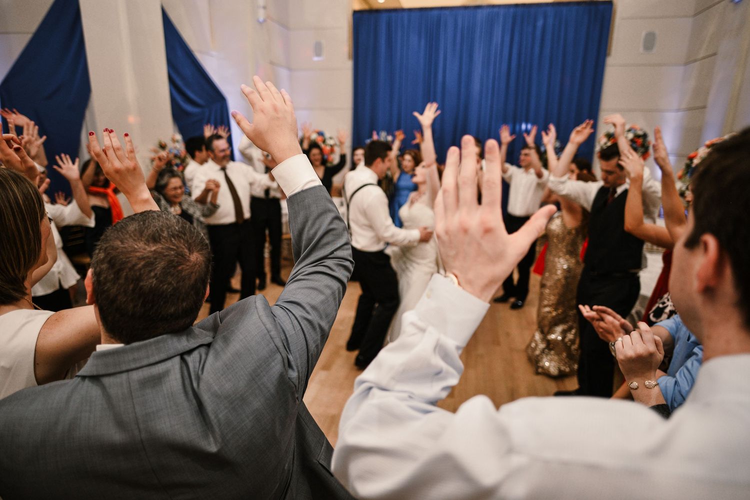 Wedding guests raise their hands on the dance floor during a lively wedding reception celebration.