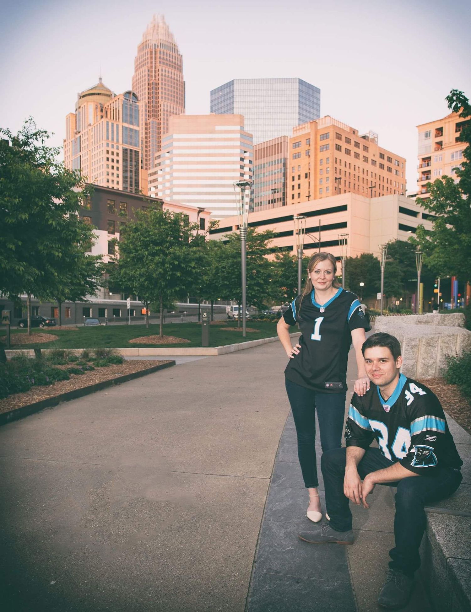 Couple poses in Carolina Panthers jerseys with Charlotte city skyline backdrop.