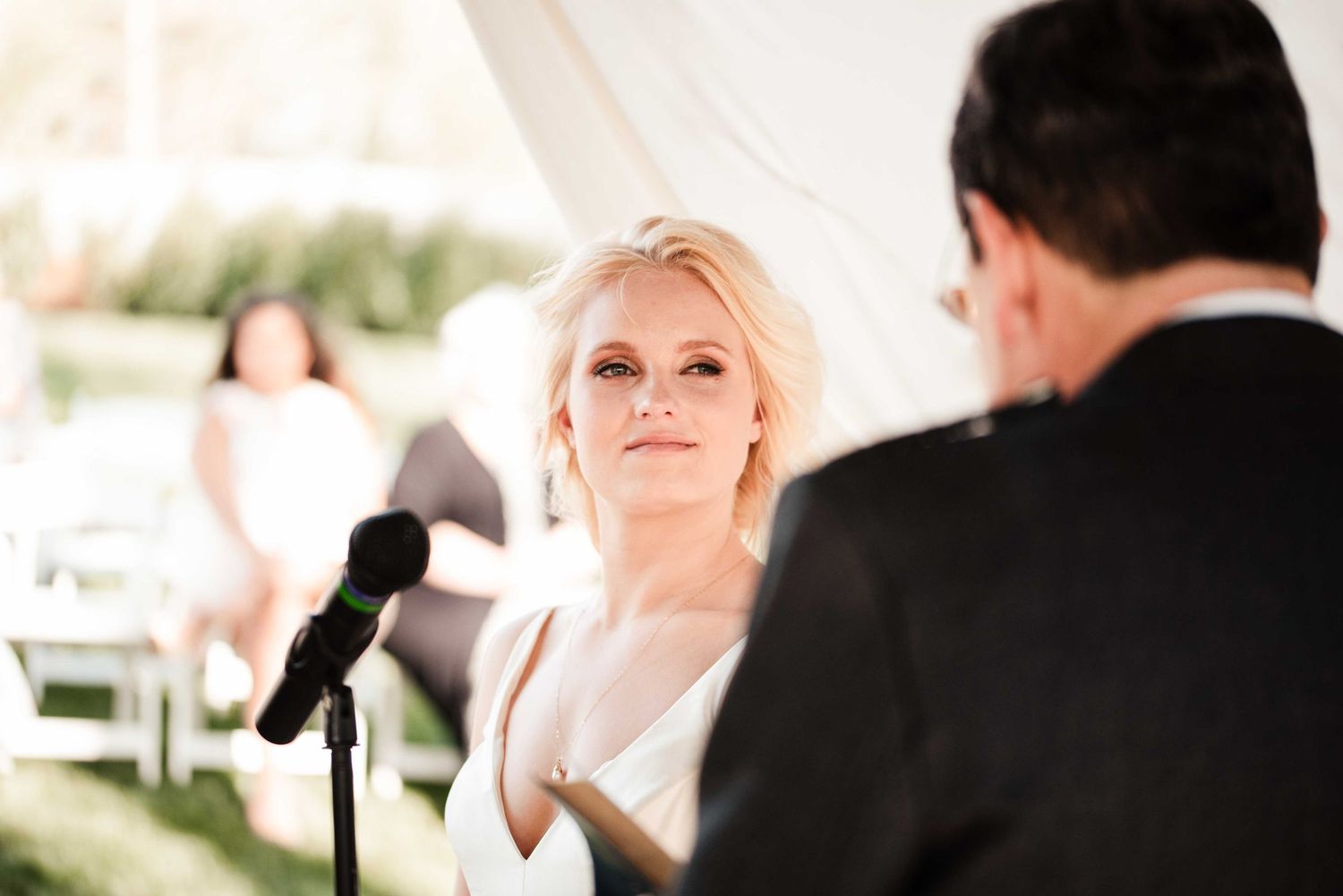 Bride gazing lovingly at groom during outdoor wedding ceremony under white tent.