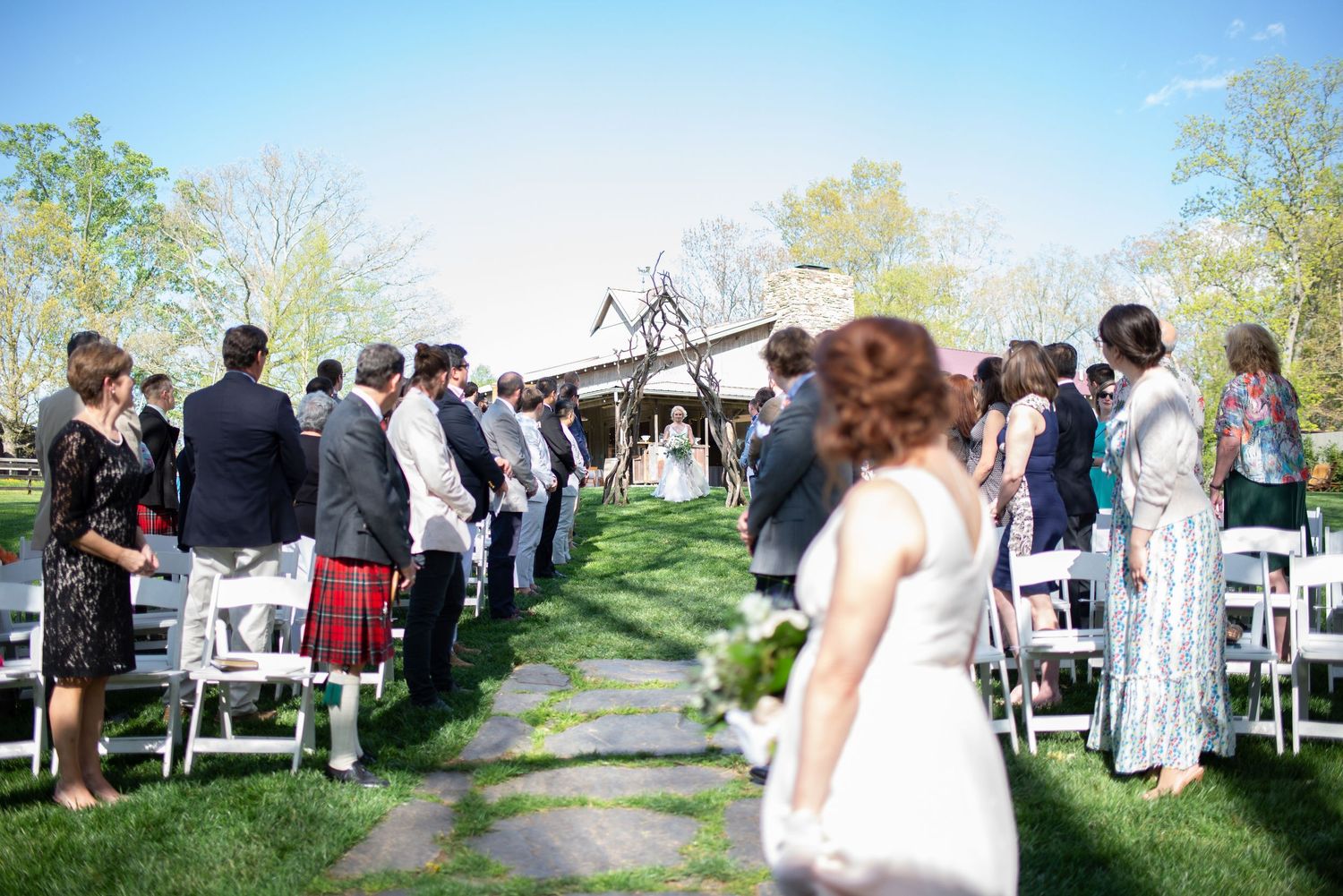 Guests seated in white chairs at outdoor wedding ceremony on sunny spring day.