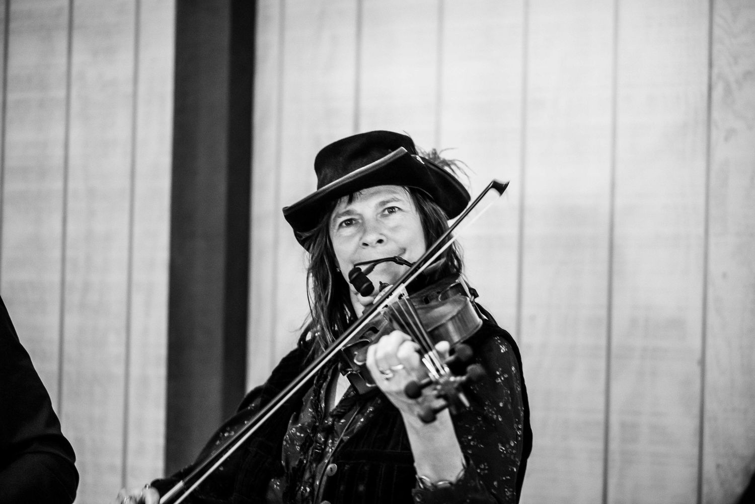 Female violinist wearing a black hat performs passionately outdoors in black and white photo.