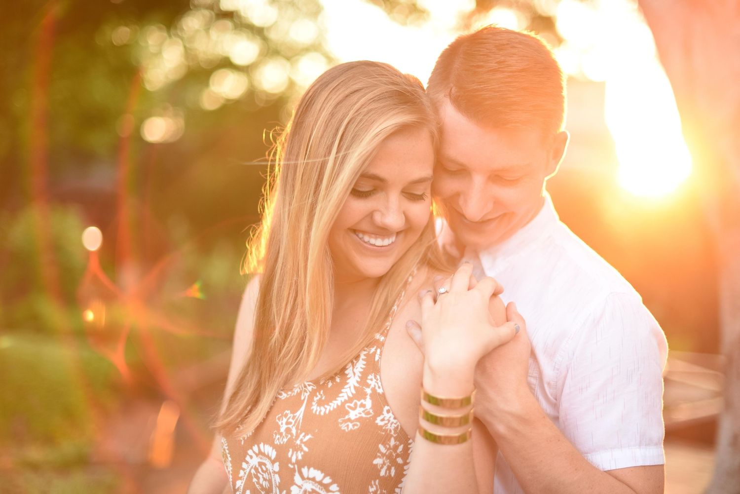 Happy blonde woman smiling as man embraces her from behind in warm golden sunset light.